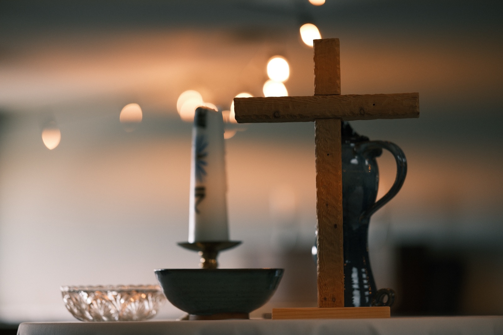 Hand-carved wooden cross, candle, and pottery on a communion table in warm light