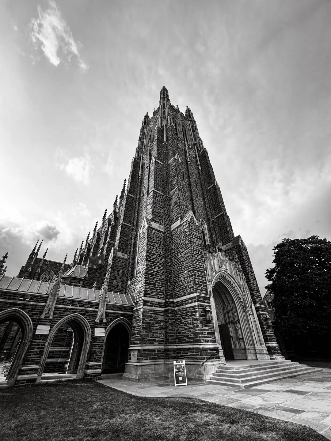Duke Chapel's Gothic tower seen from below against a clouded sky, black and white