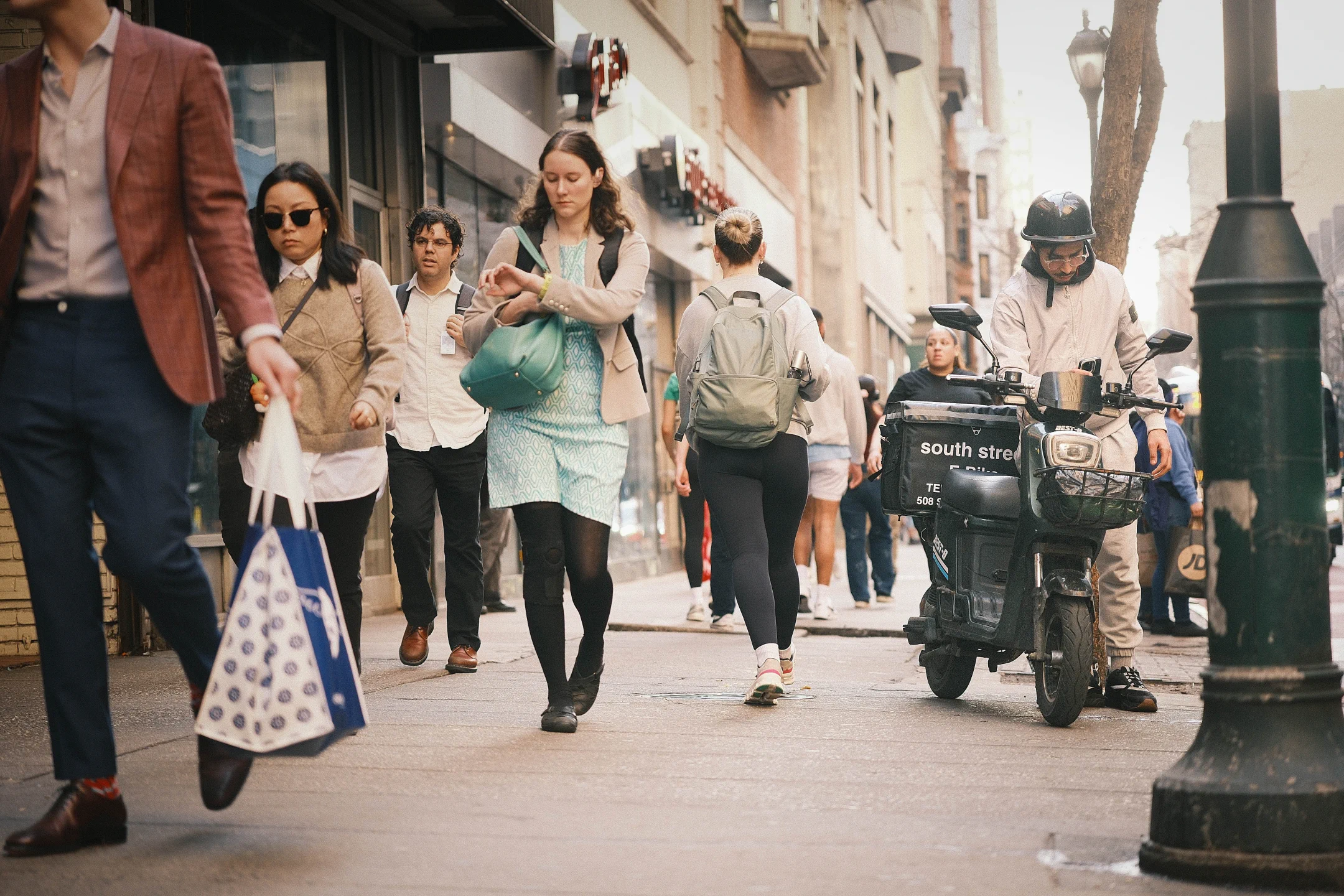 Pedestrians and a hand truck crowding a sunlit Philadelphia sidewalk