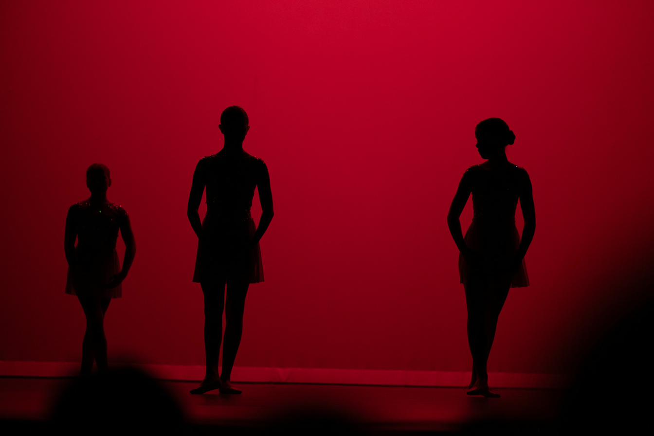 Three dancers silhouetted against a deep red stage wash